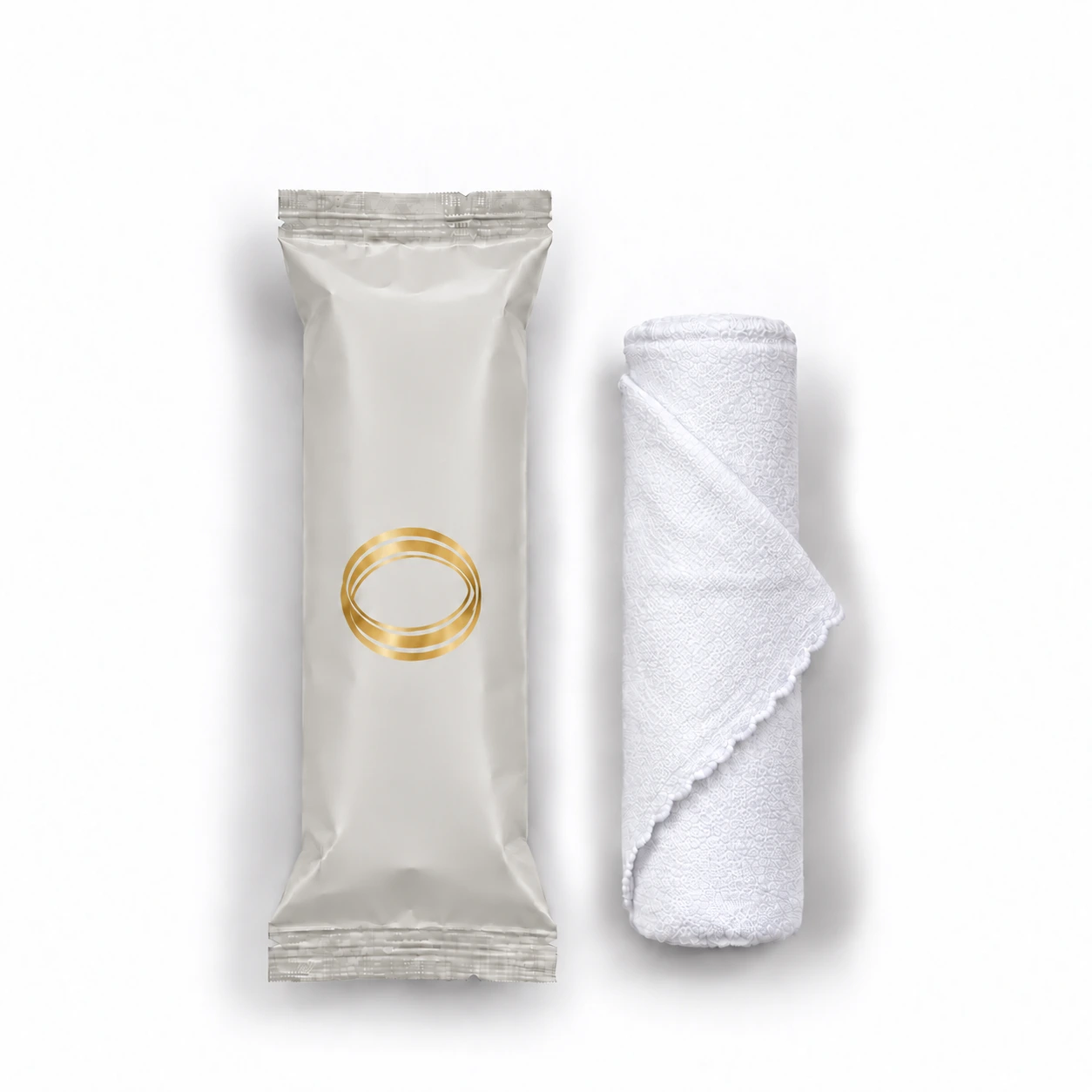Unscented oshibori towel in warm gray packaging beside the rolled white microfiber towel