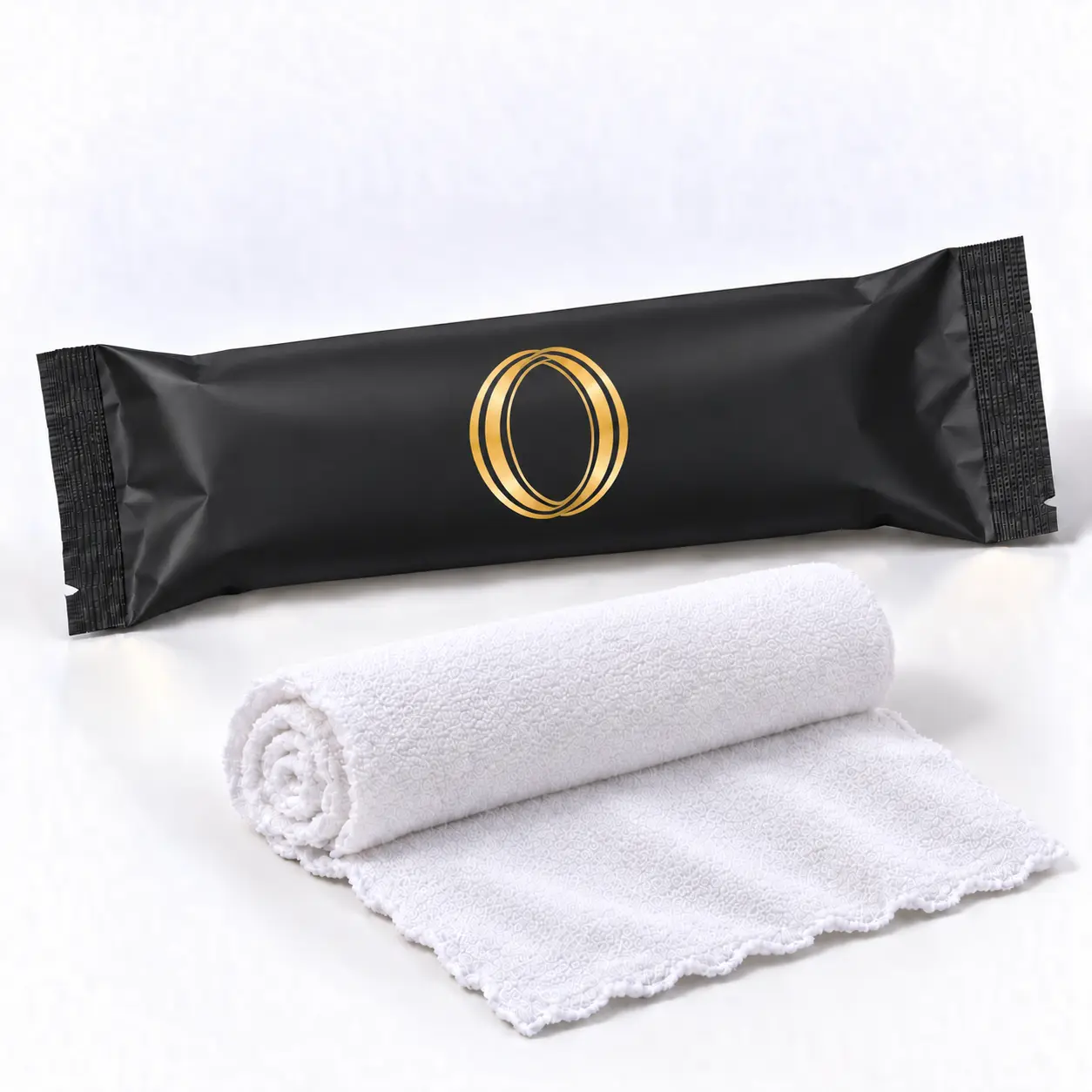 Green Tea oshibori towel in matte black packaging laid flat beside the rolled white microfiber towel